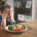 Une enfant se cache les yeux et ne mange pas ses légumes