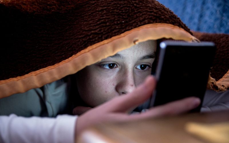 Un adolescent sur son téléphone est caché sous les draps