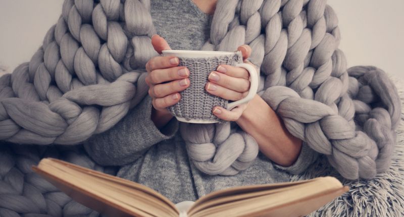 Une femme lit un livre et tient un mug pour gérer ses émotions