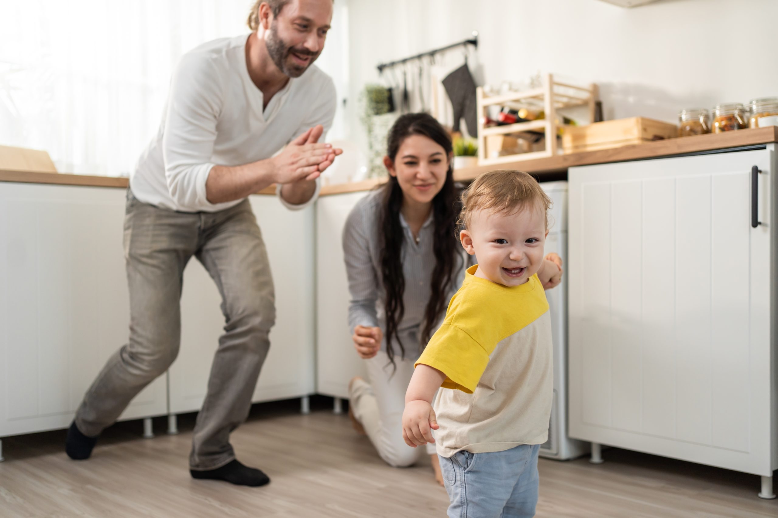 un couple de parents encourage son enfant qui fait ses premiers pas