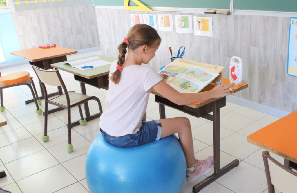 Elève assise à son bureau sur un ballon en train de faire ses devoirs.