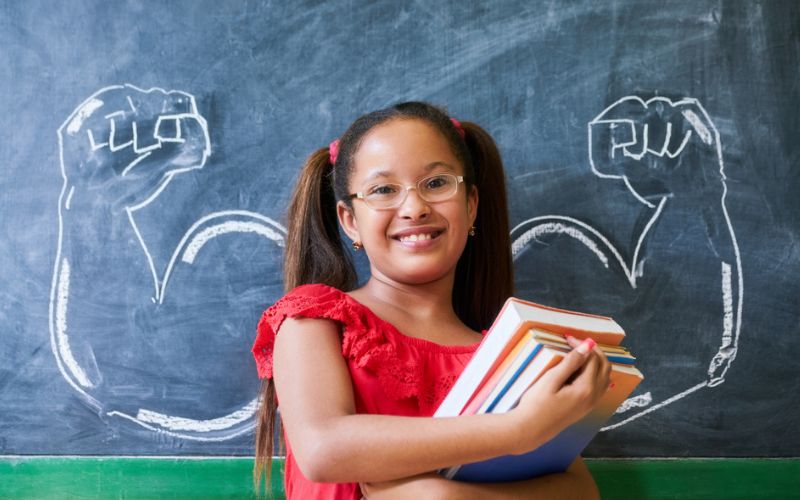 Une jeune fille devant un tableau avec des bras musclés dessinés à la craie