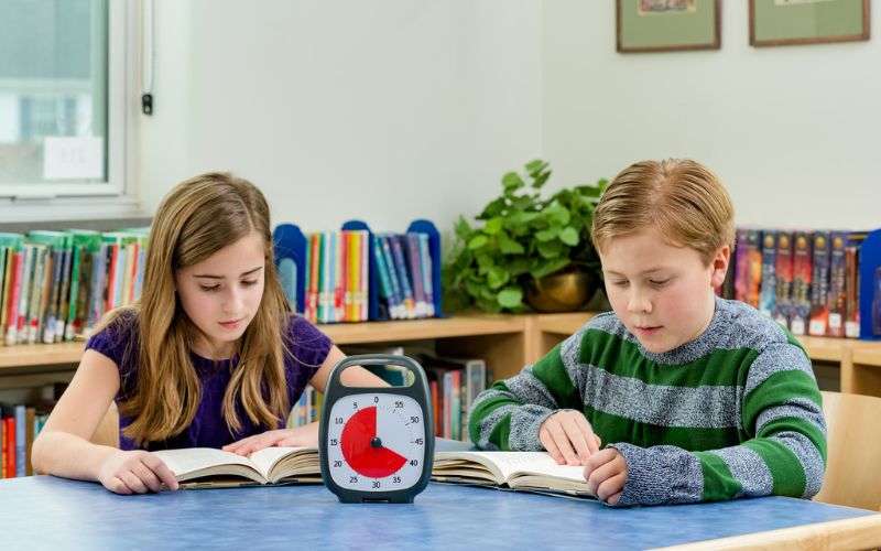 Deux élèves lisent. Un Time Timer est posé entre les deux sur une table.