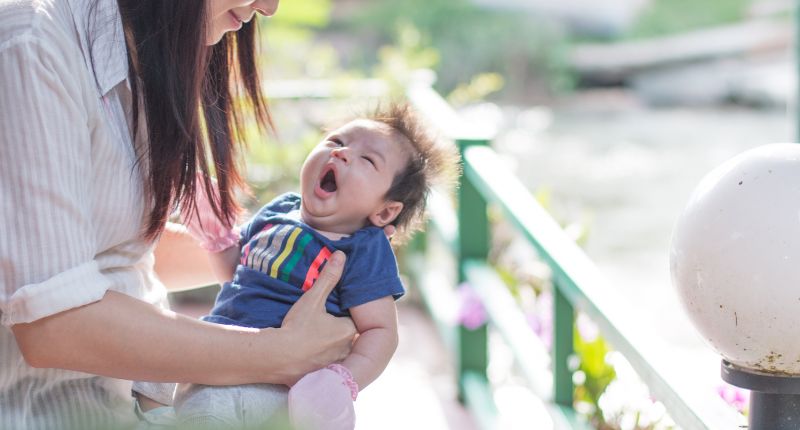 Un bébé baille dans les bras de sa mère