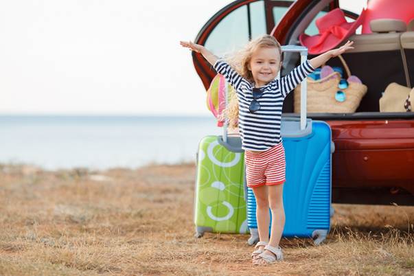 Petite fille levant les bras de joie en vacances devant deux valises en exterieur