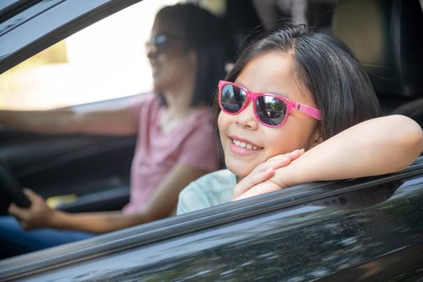 Petite fille avec lunettes de soleil rose en passager dans une voiture avec sa mère qui conduit. Elles sourient