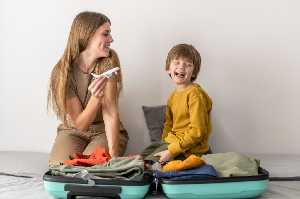 Une mère et son enfant faisant leur valise. La mère joue avec un avion en modèle réduit pour illustrer un départ en vacances