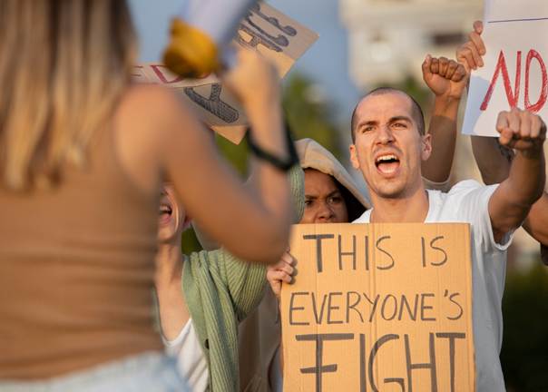 Image d'une manifestation où un homme porte une pancarte avec écrit en anglais "La lutte est à tout le monde"