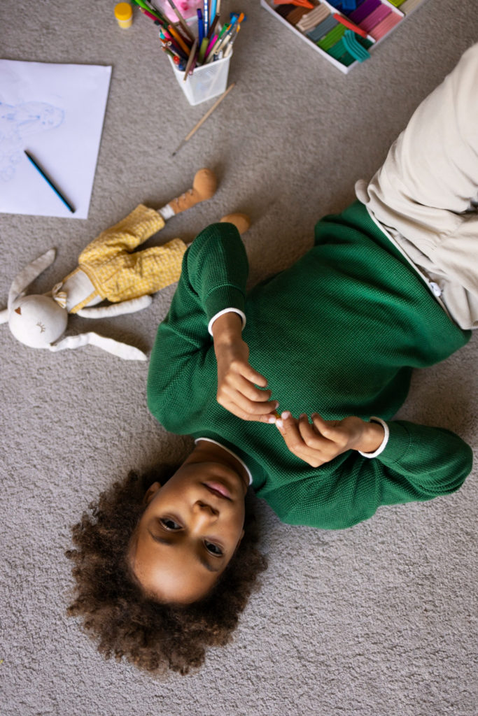 Enfant allongé sur le sol de sa chambre à côté de son doudou