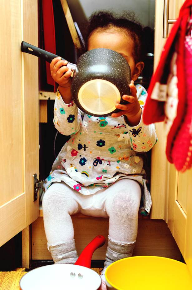 Jeune enfant jouant avec une casserole dans un placard